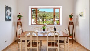 A dining area with a wooden table, white chairs, and a view of a hillside through a window. - Holiday Home ‘Maria Dolores’ with Mountain View, Wi-Fi, Garden & Terrace (HARIA)