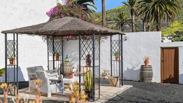 A covered outdoor seating area with chairs and tables, surrounded by potted plants and a white wall. - Holiday Home ‘Maria Dolores’ with Mountain View, Wi-Fi, Garden & Terrace (HARIA)