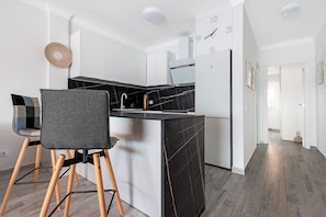 A modern kitchen with a black marble countertop, white cabinets, a built-in oven, and a clock on the wall.