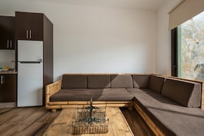 A modern living space with a wooden sectional sofa, a kitchen area, and a large window.