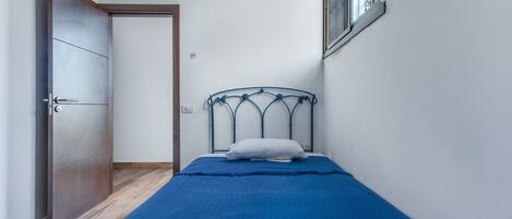 Un dormitorio con cama, puerta, ventana y una lámpara fijada a la pared.