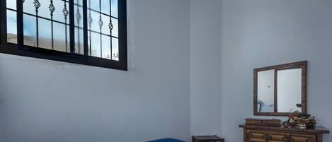 A bedroom with a bed, a dresser, a mirror, and a window with metal bars.