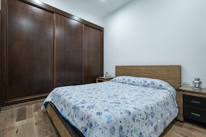 A bedroom with a bed, wooden wardrobe, bedside table, and a nightstand.