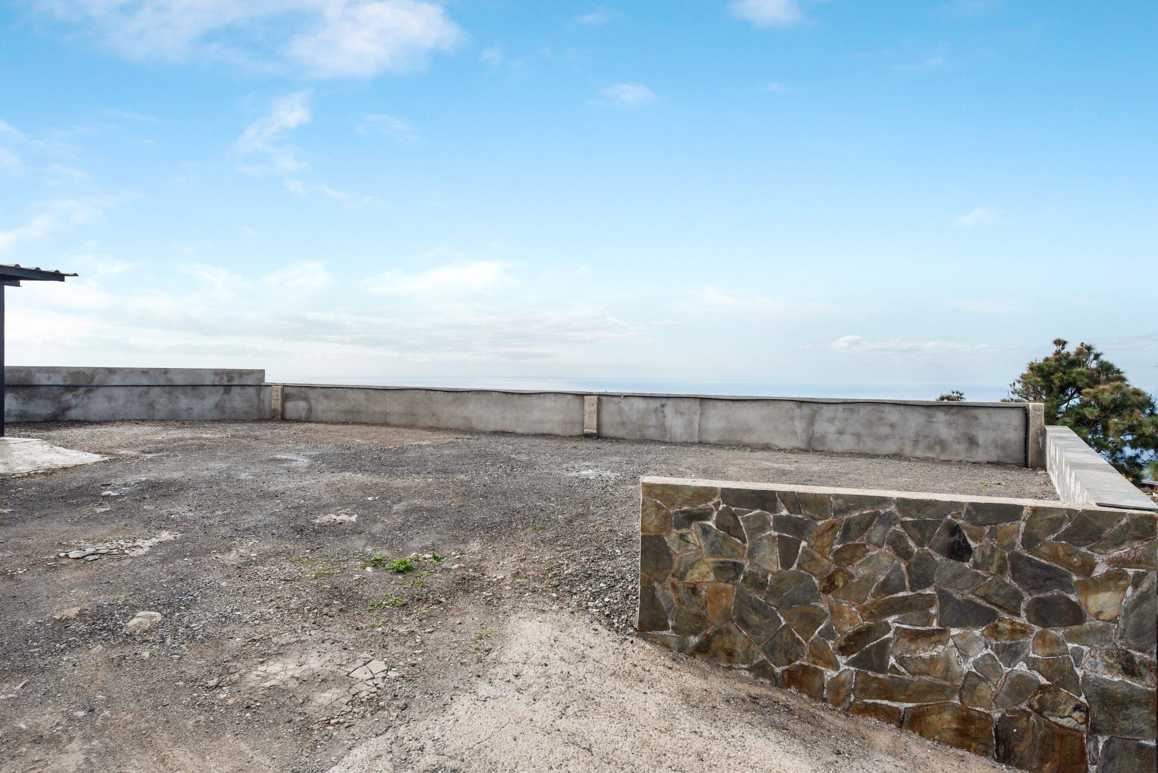 A rooftop terrace with a view of the horizon, a stone wall, and a concrete barrier.
