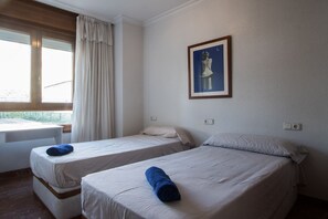 Una habitació amb dos llits individuals, una finestra amb cortines, una taula petita i un quadre al mur.