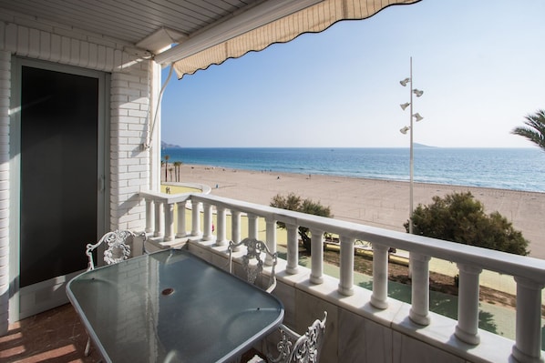 A balcony with a glass table and chairs, overlooking a beach with a clear view of the sea and distant mountains. - VERALUX 2. (BENIDORM)