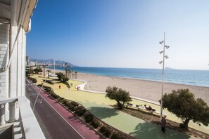 Un balcó amb vista a una platja, un camí per a vianants i un paisatge urbà al fons.