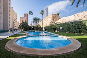A swimming pool with a curved edge, surrounded by a grassy area and palm trees. - VERALUX 2. (BENIDORM)
