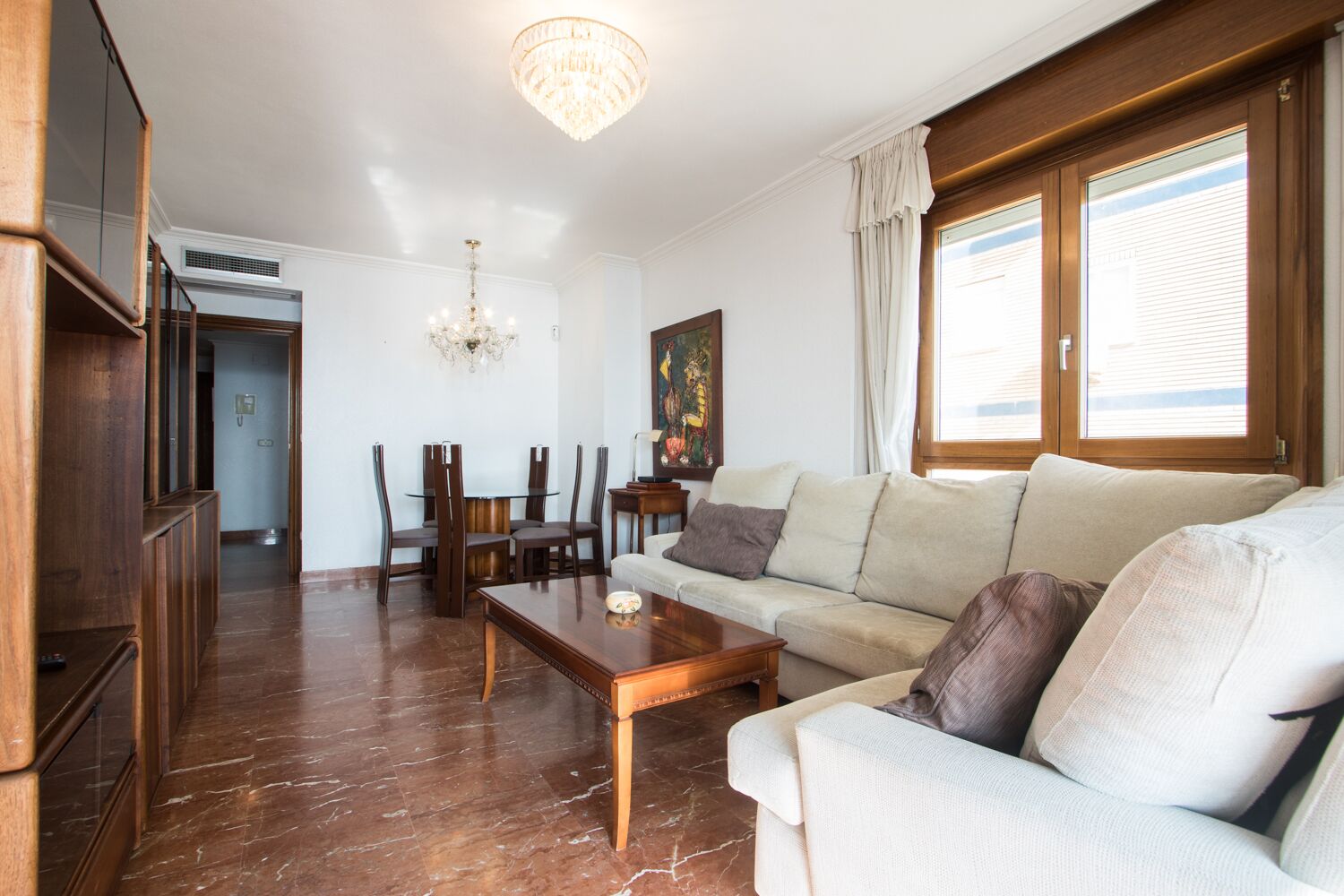 Amplia sala de estar con una mesa de centro de madera, un sofá color beige y un comedor con mesa y sillas de madera.