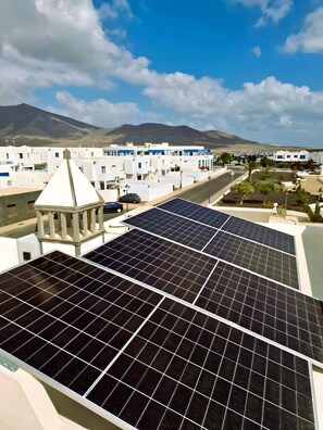 A rooftop with solar panels, a white building with a pyramid-shaped structure, and a mountainous landscape in the background. - Vacation Home 'Casa De Pato' with Private Terrace, Private Garden and Wi-Fi (Playa Blanca)