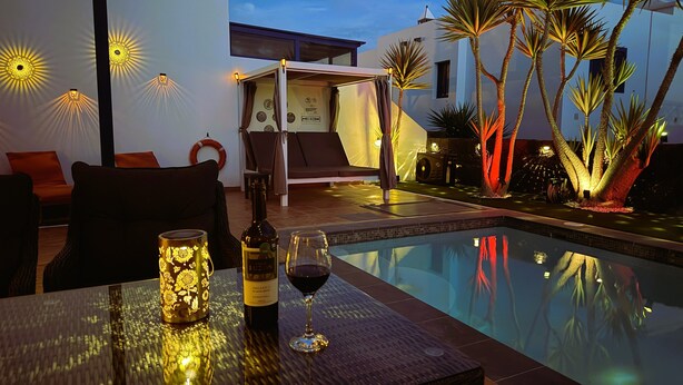 Ein Poolbereich mit Tisch, Stühlen, einer Weinflasche und einem Weinglas.