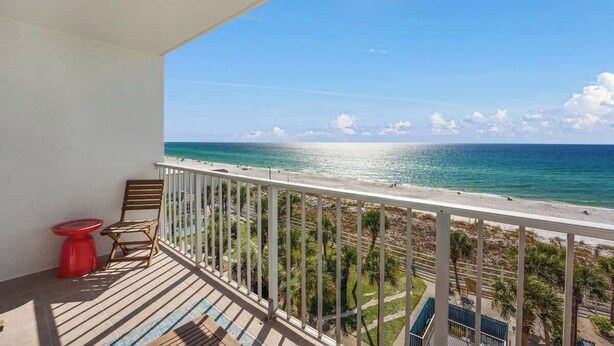 Ein Balkon mit Blick auf das Meer, ein roter Tisch und ein Holzstuhl.