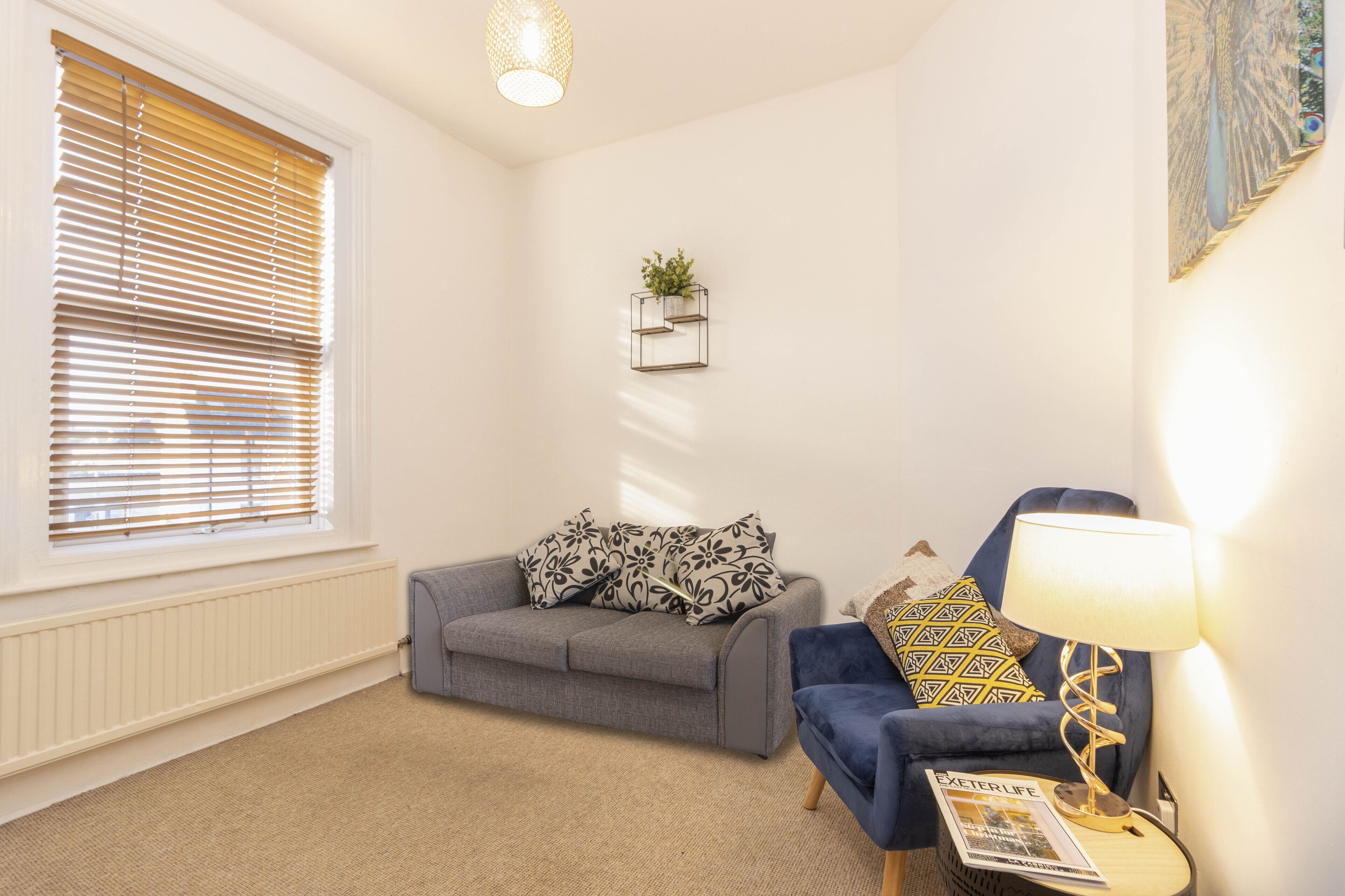 A living room with a grey sofa, a blue armchair, a lamp, and a magazine on a side table.