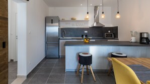 Una cocina moderna con un refrigerador de acero inoxidable, un microondas y una cafetera. Hay taburetes y una mesa de madera.