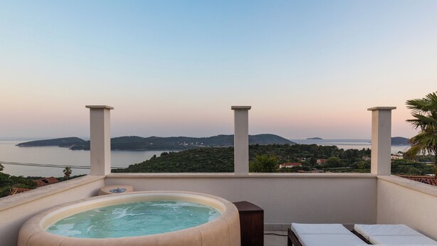 Un jacuzzi con sillones de descanso en un balcón con vistas panorámicas a un lago y colinas.