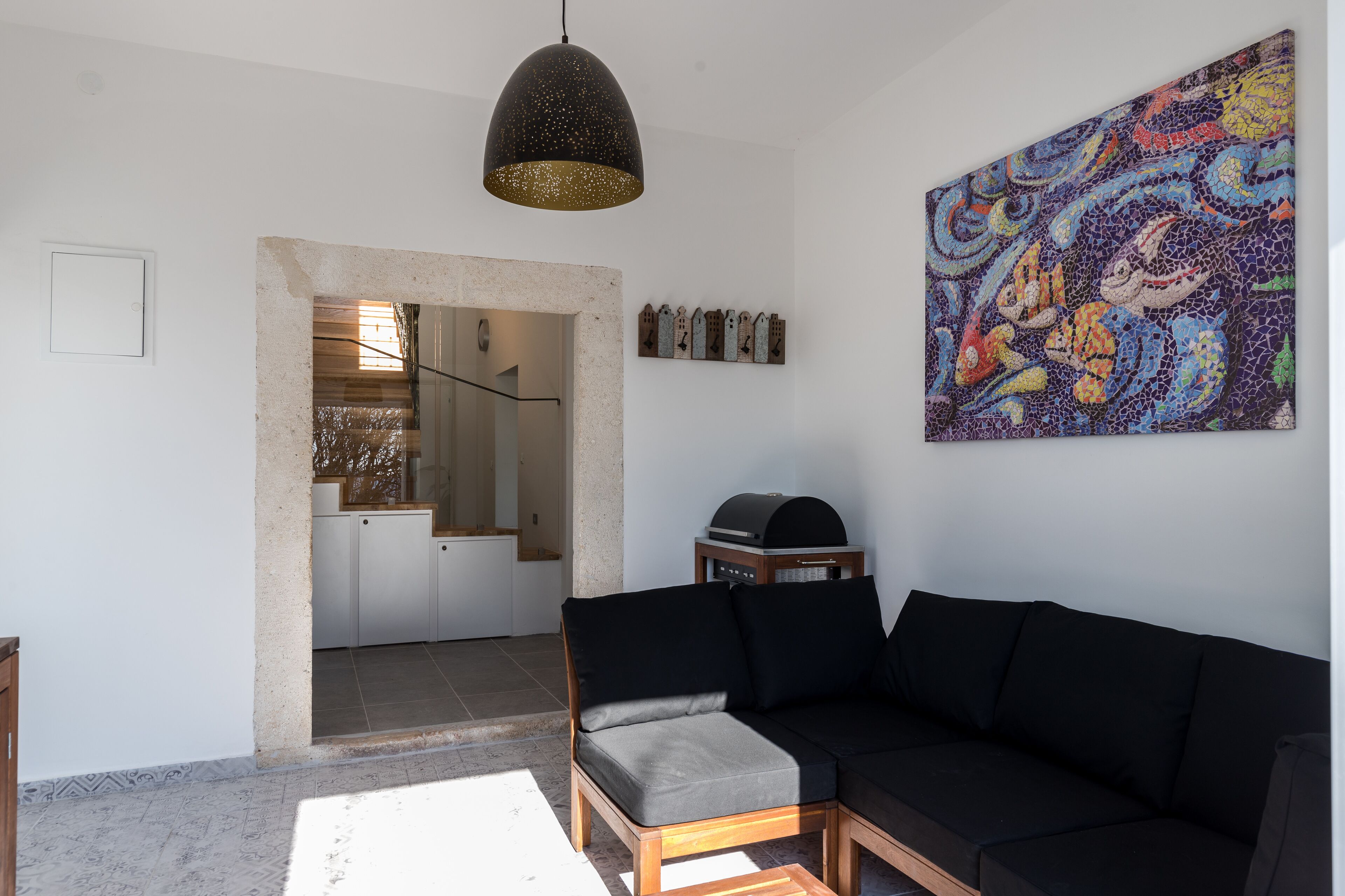 A modern living room with a black sofa, a wooden coffee table, and a large abstract painting on the wall.