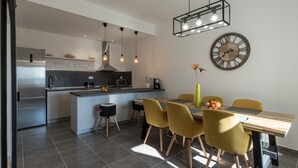 Una cocina moderna con una isla central, electrodomésticos de acero inoxidable, iluminación colgante y un comedor con sillas amarillas y una mesa de madera.
