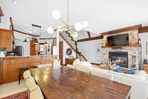 A spacious living area with a wooden dining table, white sofas, and a stone fireplace. - Le Plateau Ski In/Out w/ 3bdrs w/ Pool Access (Mont-Tremblant)