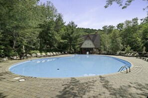 A swimming pool with lounge chairs and a building in the background. - Le Plateau Ski In/Out w/ 3bdrs w/ Pool Access (Mont-Tremblant)
