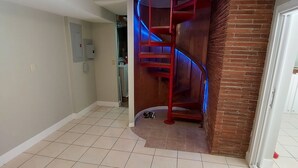 Una habitación amplia con suelo de baldosas, pared de ladrillo decorativa y una escalera espiral roja.