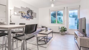 A modern kitchen with a dining area, a sofa, a TV, and artwork on the wall.