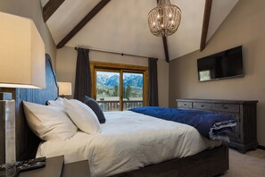 A bedroom with a large bed, a TV, a dresser, and a window with a mountain view.