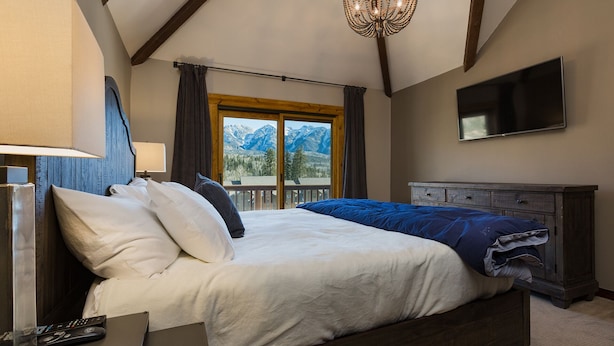 Une chambre avec un grand lit, une télévision, une commode et une fenêtre donnant sur la montagne.