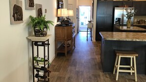 A modern kitchen with dark cabinetry, a central island, and a bar area. There are decorative wall art pieces and a potted plant on the counter.