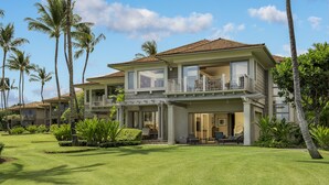 Une maison à deux étages dotée d’un balcon, entourée de palmiers et d’une pelouse bien entretenue.