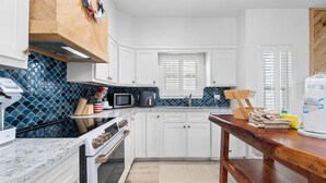 A modern kitchen with white cabinets, a black stove, a microwave, and a coffee maker.