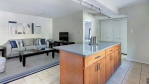 Una cocina moderna con una isla grande, un área de comedor con sofá y mesa de centro, y un televisor en la sala de estar.