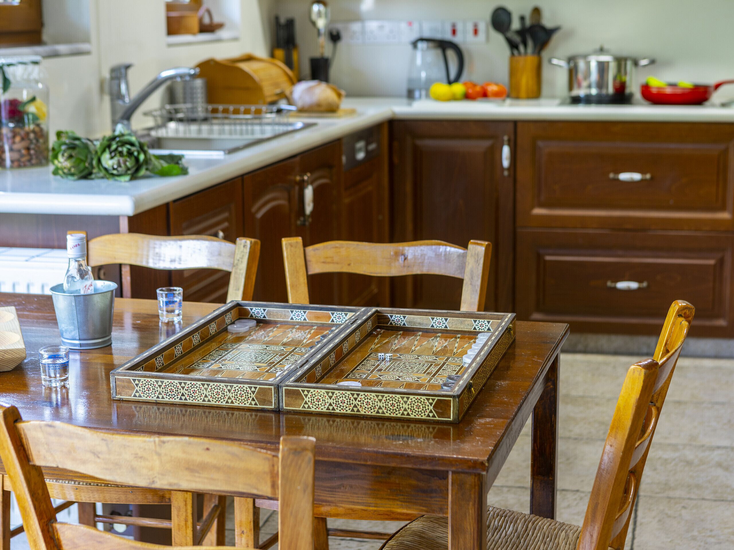A wooden dining table with a patterned tray, chairs, and a kitchen in the background.