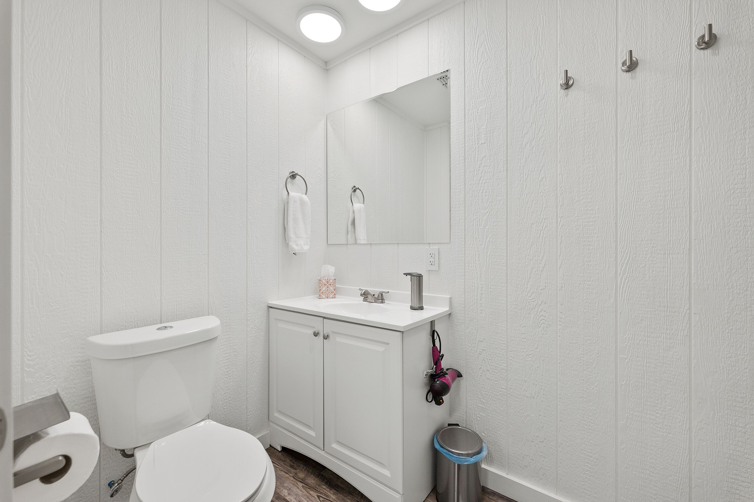 A bathroom with a toilet, sink, mirror, and a trash bin.