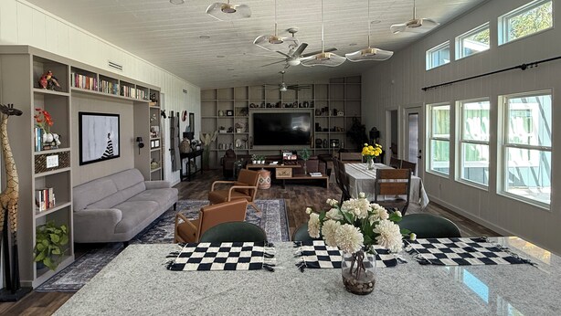 A spacious living room with a large TV, comfortable seating, and a bookshelf filled with books and decorative items.