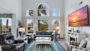A spacious living room with a fireplace, a large TV, and a view of the outdoors through large windows. - 2 Golf Carts ~ Golf Course Views ~ Lake Views (Miramar Beach)