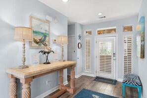 A hallway with a wooden console table, two lamps, a framed painting, and a bench.