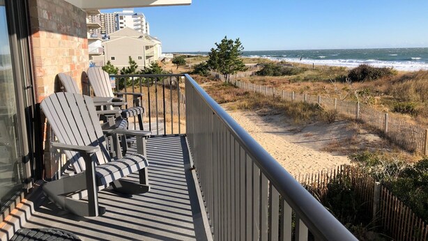 Ein Balkon mit zwei Adirondack-Stühlen, einem kleinen Tisch und Blick auf Strand und Meer.