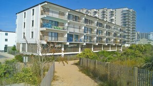Ein mehrstöckiges Hotel mit Balkonen, einem Sandweg und einem Holzzaun.