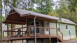 Une cabane en bois dotée d’un porche, d’un espace abrité et d’une petite dépendance attenante.