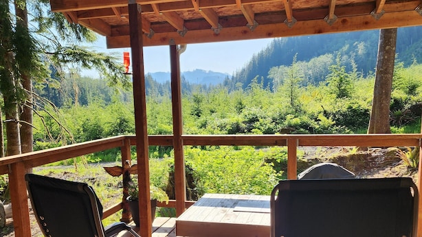 Une terrasse en bois avec deux chaises et une table, donnant sur une vallée boisée.
