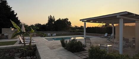 A patio area with a pool, lounge chairs, and a covered seating area.