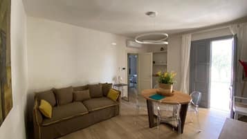 A modern living room with a sofa, a dining table with chairs, and a ceiling light fixture.
