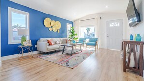 Uma sala de estar com parede azul, um sofá branco, uma mesa de centro e uma TV fixada na parede.