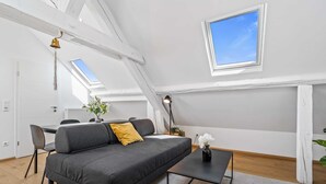 Een moderne woonkamer met een grijze bank, een klein zwart tafeltje en een raam met uitzicht op de lucht.