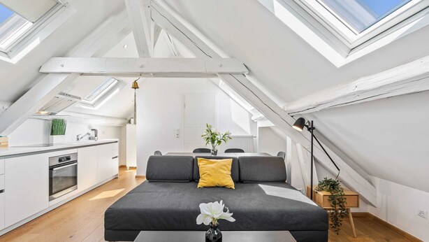Een modern loft appartement met een keuken, eethoek en een grote grijze bank met een geel kussen.