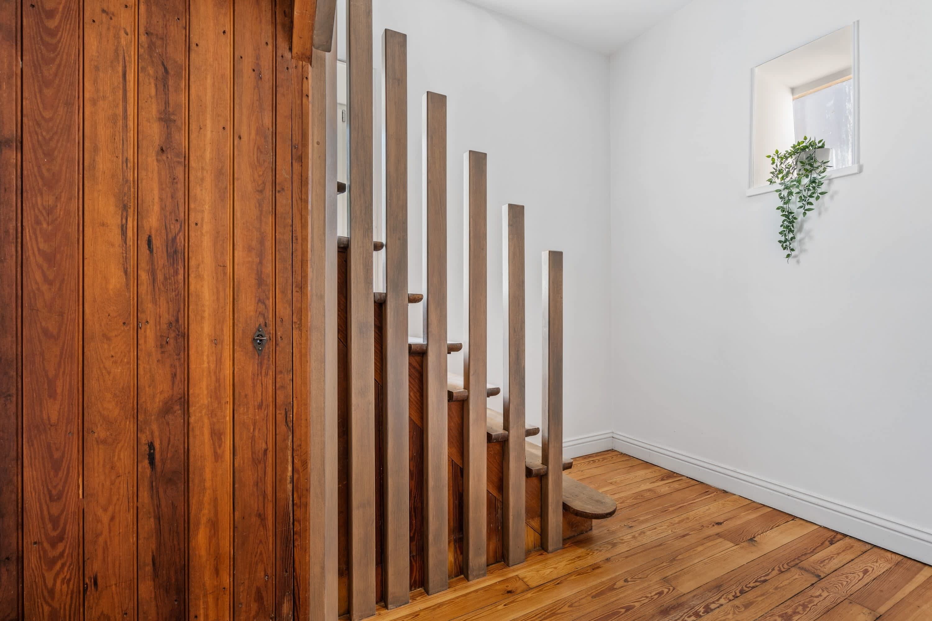 A wooden staircase with a white wall and a small window with a plant.