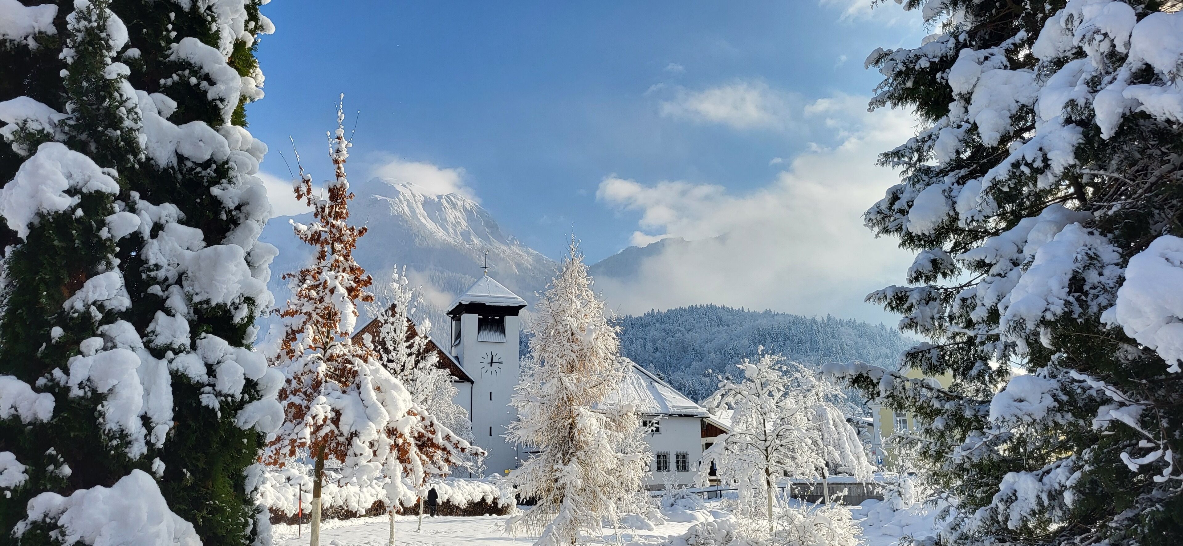 A snow-covered village with a church, surrounded by trees and mountains.