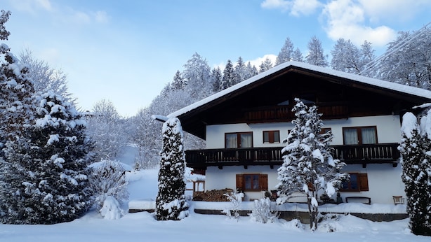 A two-story chalet with a wooden balcony, surrounded by snow-covered trees and a mountain backdrop. - Ferienwohnung 2 Personen, 50 qm, - Hoher Göll, Sep. Schlafzimmer, Balkon (Schönau am Königssee)