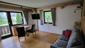 A cozy room with a wooden ceiling, a sofa with a patterned cover, a dining table with chairs, and a TV mounted on the wall. - Ferienwohnung 2 Personen, 50 qm, - Hoher Göll, Sep. Schlafzimmer, Balkon (Schönau am Königssee)