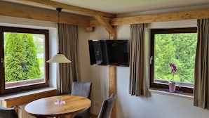 A room with a wooden ceiling, a TV mounted on the wall, a round wooden table with chairs, and a window with curtains. - Ferienwohnung 2 Personen, 50 qm, - Hoher Göll, Sep. Schlafzimmer, Balkon (Schönau am Königssee)